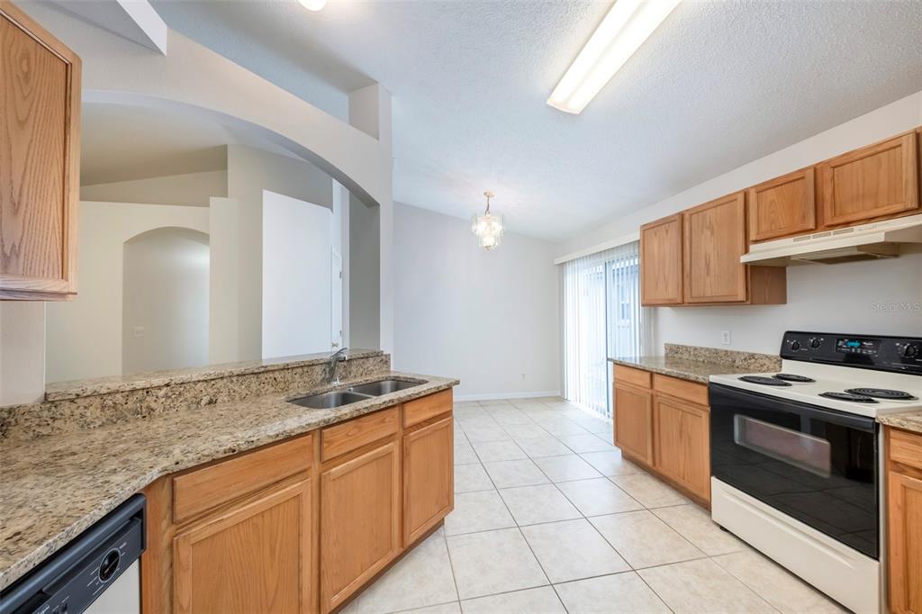A kitchen features light wood cabinets, granite countertops, tile flooring, and a dining area — 10109 VISTA COVE LANE, ORLANDO, FL