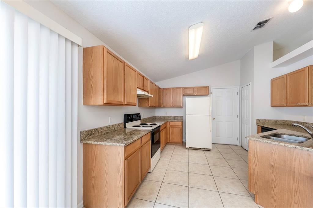 A kitchen features light wood cabinets, granite countertops, white appliances, and beige tile flooring — 10109 VISTA COVE LANE, ORLANDO, FL