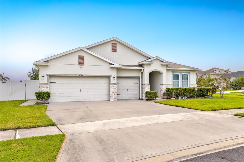 A single-story house with a three-car garage, light-colored stucco exterior, and stone accents — 1799 RANGER HIGHLANDS ROAD, KISSIMMEE, FL
