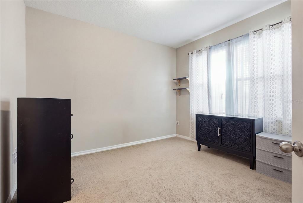 A carpeted bedroom features beige walls, a window with sheer curtains, and two pieces of furniture — 1799 RANGER HIGHLANDS ROAD, KISSIMMEE, FL