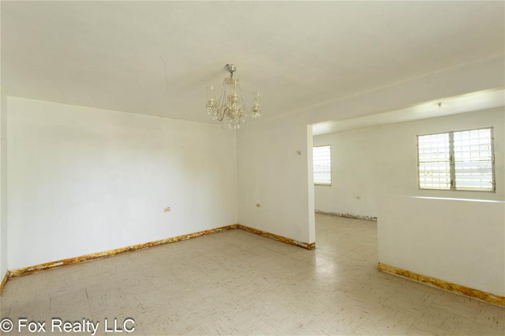 An empty room features white walls, a crystal chandelier, and light-colored tile flooring — Solar B AVENIDA MARIA BETTEGA, AGUADILLA, PR