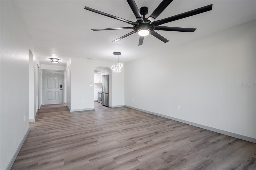 An empty room with light wood-look flooring, white walls, a ceiling fan, and a kitchen view — 2395 HARBOR BOULEVARD UNIT 314, PORT CHARLOTTE, FL