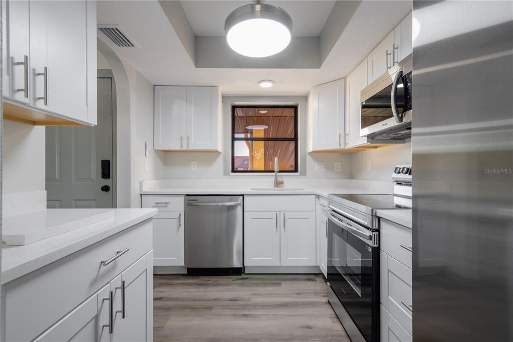 A modern kitchen features white cabinets, stainless steel appliances, and wood-look flooring — 2395 HARBOR BOULEVARD UNIT 314, PORT CHARLOTTE, FL