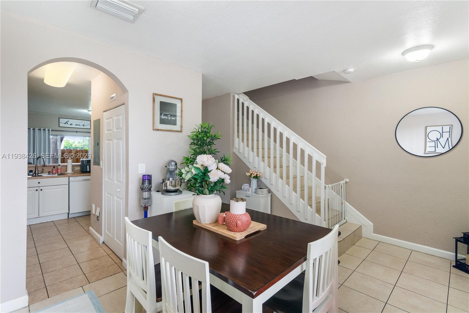 A dining area with a dark wood table and white chairs sits beside a staircase — 1420 NE 33rd Ave # 15, Homestead FL 33033, HOMESTEAD, FL