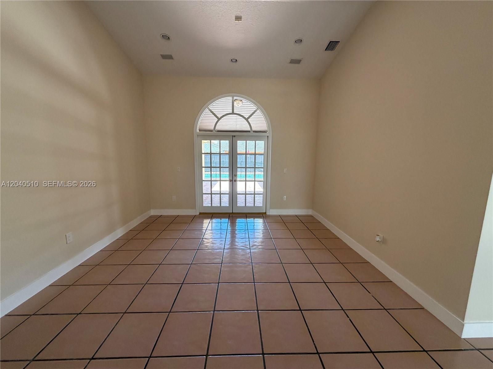 An empty room features tan tile flooring, beige walls, and a glass-paned double door — 15836 SW 144th Pl, Miami FL 33177, MIAMI, FL