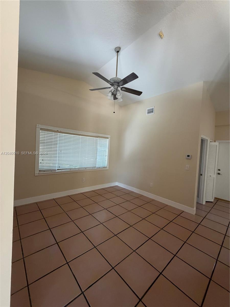 An empty room features beige walls, a vaulted ceiling with a fan, and tiled floors — 15836 SW 144th Pl, Miami FL 33177, MIAMI, FL