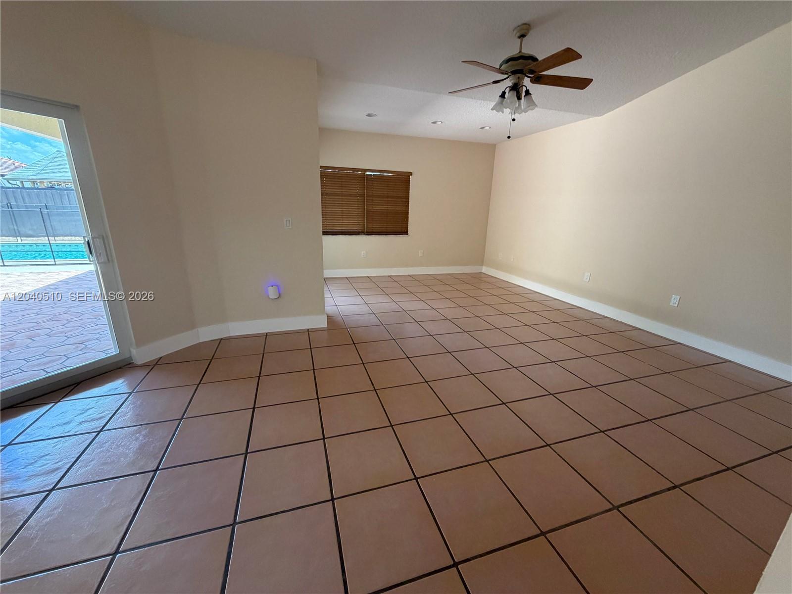 An empty room features beige walls, tile flooring, a ceiling fan, and a sliding glass door — 15836 SW 144th Pl, Miami FL 33177, MIAMI, FL