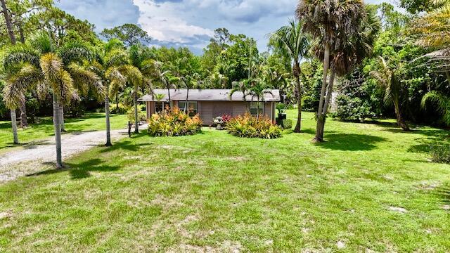 A single-story house sits on a grassy lot surrounded by palm trees and lush vegetation — 13559 24th Court N, Loxahatchee FL 33470, LOXAHATCHEE, FL