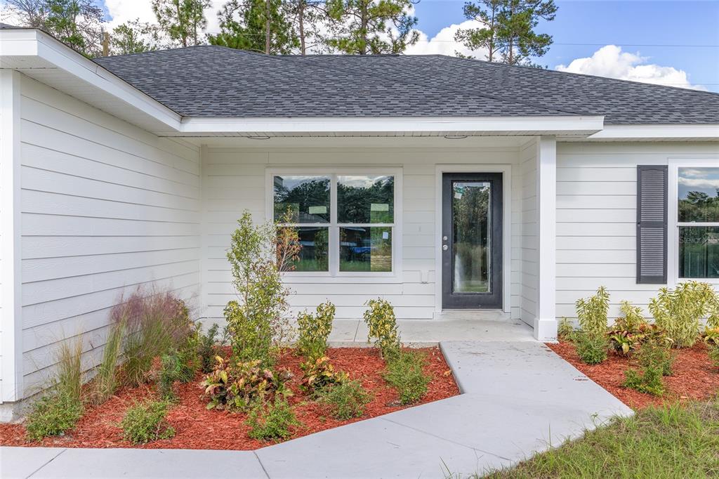 The exterior of a white house features a front door, a window, and landscaped mulch — 777 MARION OAKS LANE, OCALA, FL