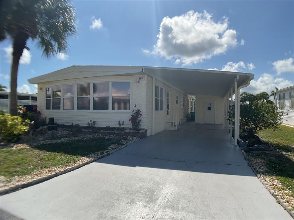 A single-story manufactured home features a light-colored exterior, a carport, and a front garden — 2100 KINGS HIGHWAY UNIT 98, PORT CHARLOTTE, FL