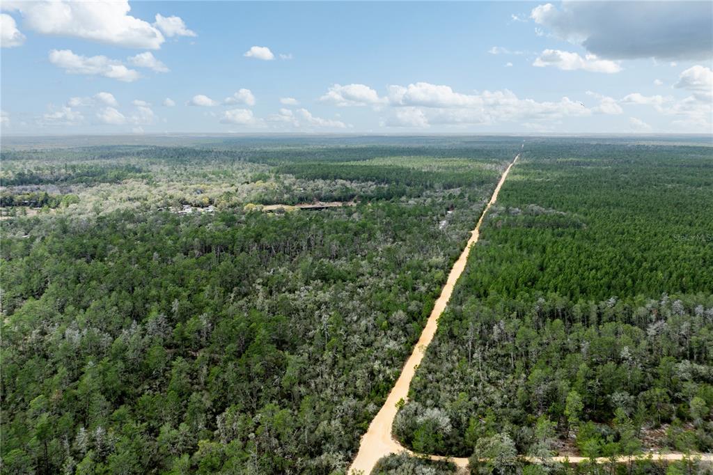 An aerial view shows a dirt road cutting through a dense, forested landscape under clouds — 0 FOREST 02, #1, SE 150TH STREET, UMATILLA, FL