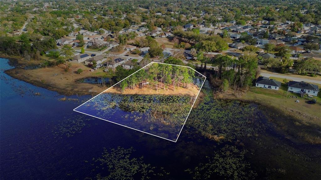An aerial view shows a wooded waterfront lot outlined in white next to a residential neighborhood — 458 HAVERSHAM ROAD, DELTONA, FL