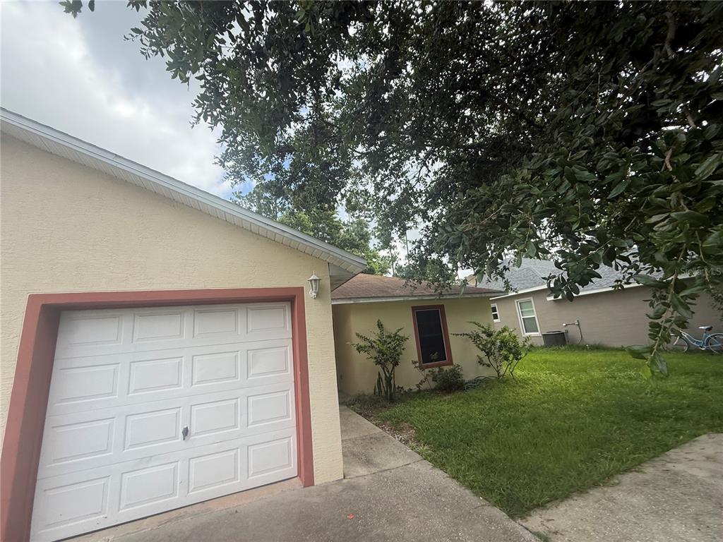 A view of a house exterior featuring a garage, a walkway, and a large tree — 49 PROVIDENCE LANE UNIT B, PALM COAST, FL