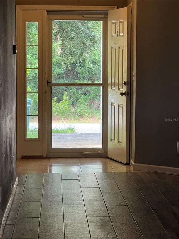 An open front door reveals a view of greenery through a storm door and sidelight — 49 PROVIDENCE LANE UNIT B, PALM COAST, FL