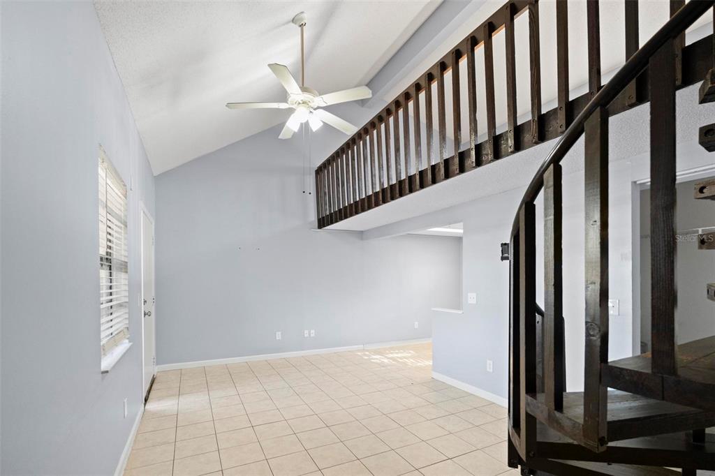 A living area features a vaulted ceiling, tile flooring, and a wooden spiral staircase — 2142 BRADFORD STREET UNIT 323, CLEARWATER, FL