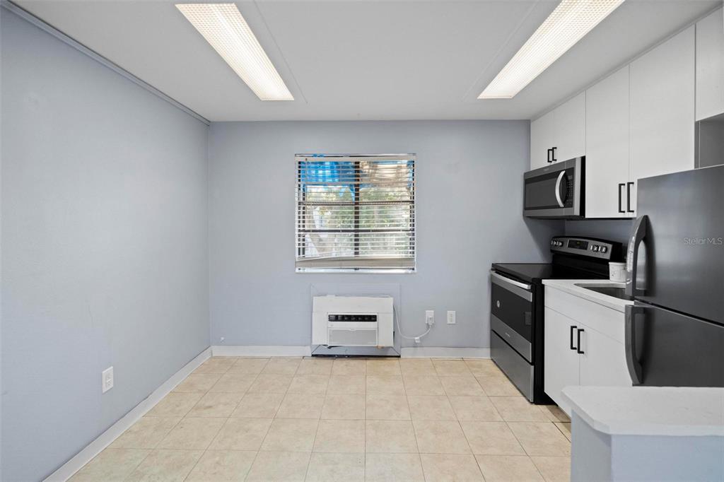 A kitchen features light blue walls, tile flooring, white cabinets, and stainless steel appliances — 2142 BRADFORD STREET UNIT 323, CLEARWATER, FL