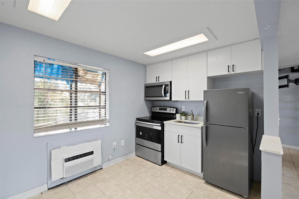 A small kitchen features white cabinets, stainless steel appliances, and a window with blinds — 2142 BRADFORD STREET UNIT 323, CLEARWATER, FL