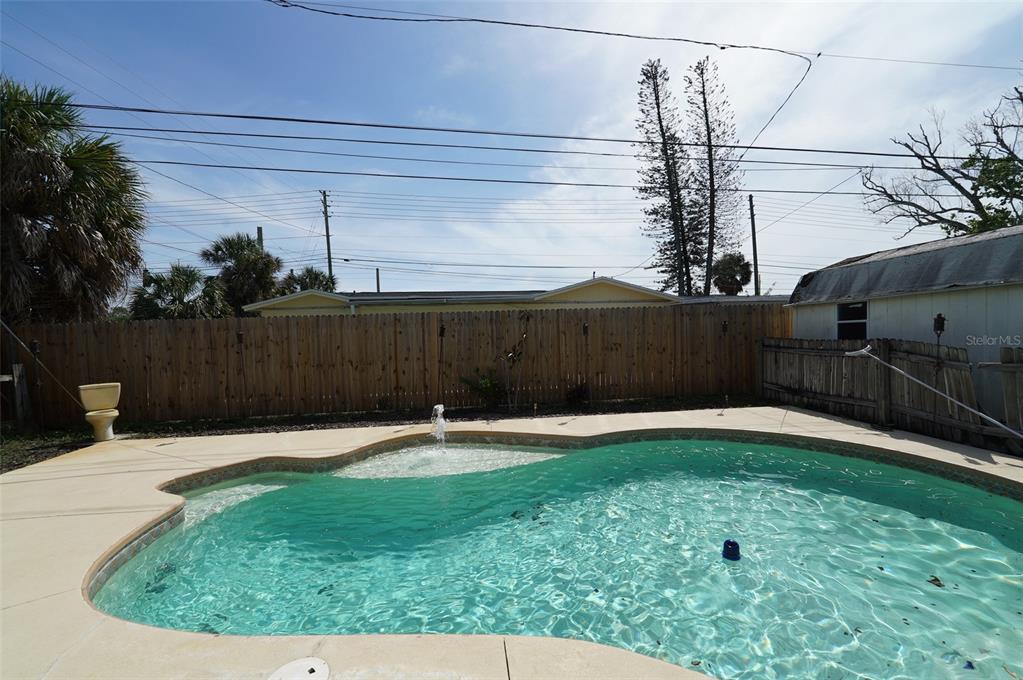 A backyard swimming pool with a fountain feature sits in front of a wooden fence — 8300 75TH AVENUE, SEMINOLE, FL