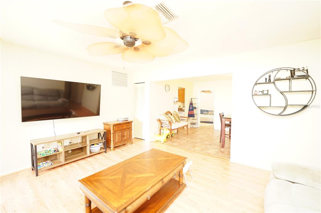 A living room features light wood flooring, a ceiling fan, and a wall-mounted television — 8300 75TH AVENUE, SEMINOLE, FL