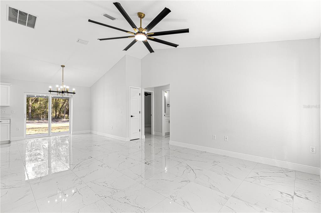 A bright, open-concept living area features white marble-look tile flooring and a vaulted ceiling — 10325 SE 125TH LANE, BELLEVIEW, FL