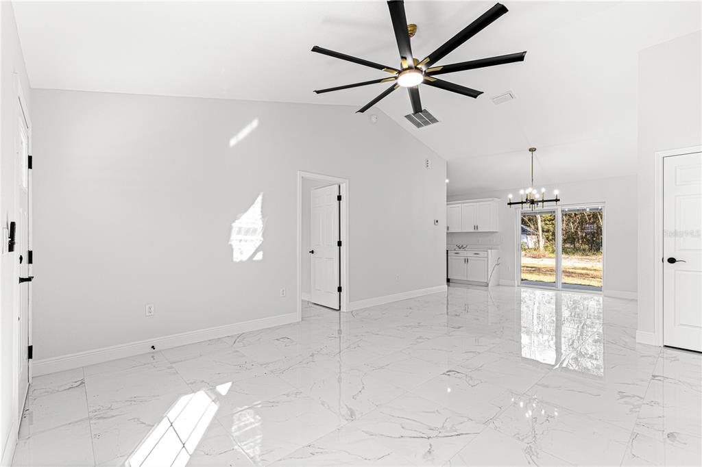 A bright, open-concept living area features white marble-look tile flooring and a vaulted ceiling — 10325 SE 125TH LANE, BELLEVIEW, FL