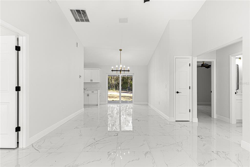 A bright dining area with white tile floors, a chandelier, and sliding glass patio doors — 10325 SE 125TH LANE, BELLEVIEW, FL