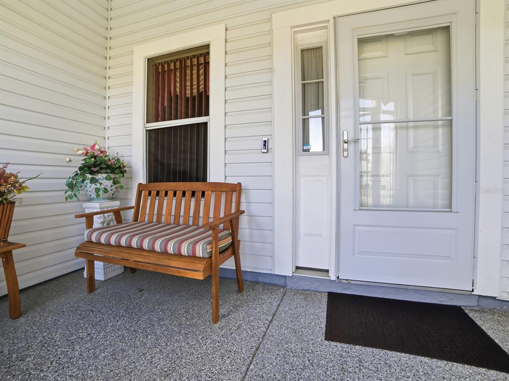 A wooden bench with a striped cushion sits on a covered porch near a door — 820 CORTEZ AVENUE, LADY LAKE, FL