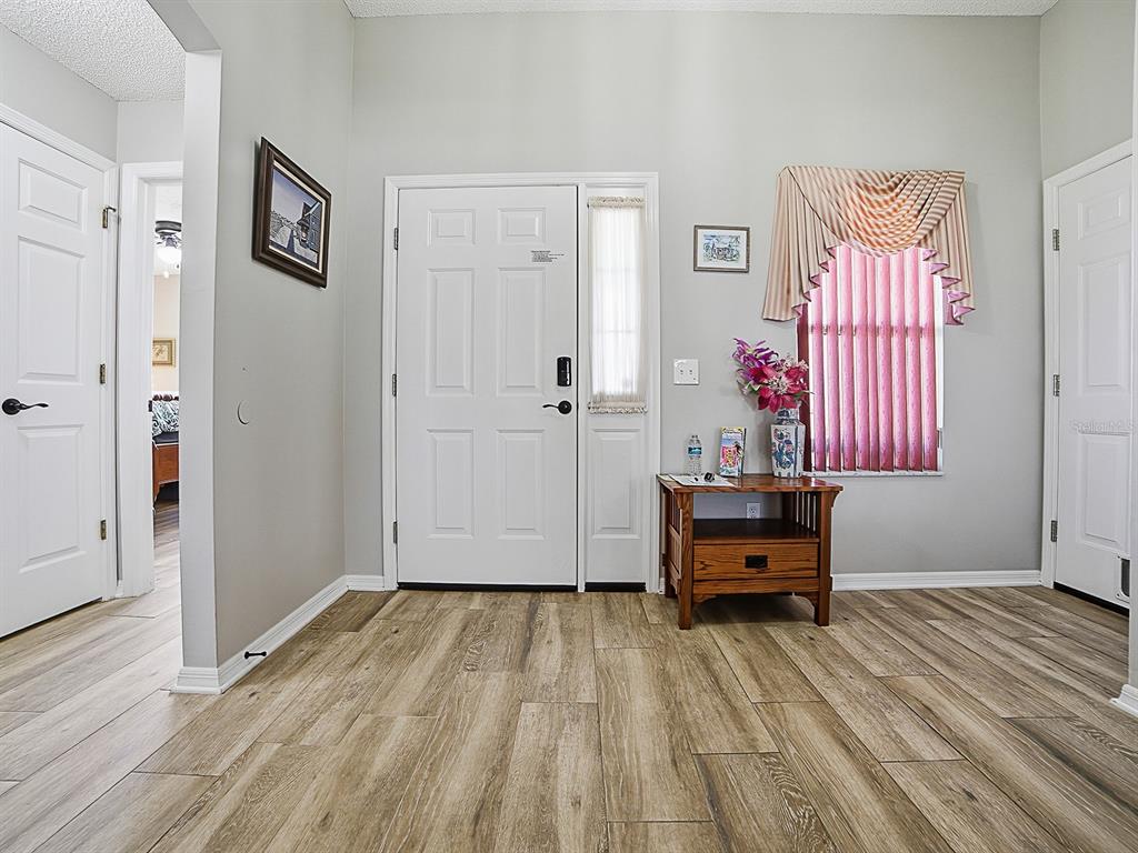 An entryway features light wood-look flooring, a white front door, and a small wooden table — 820 CORTEZ AVENUE, LADY LAKE, FL