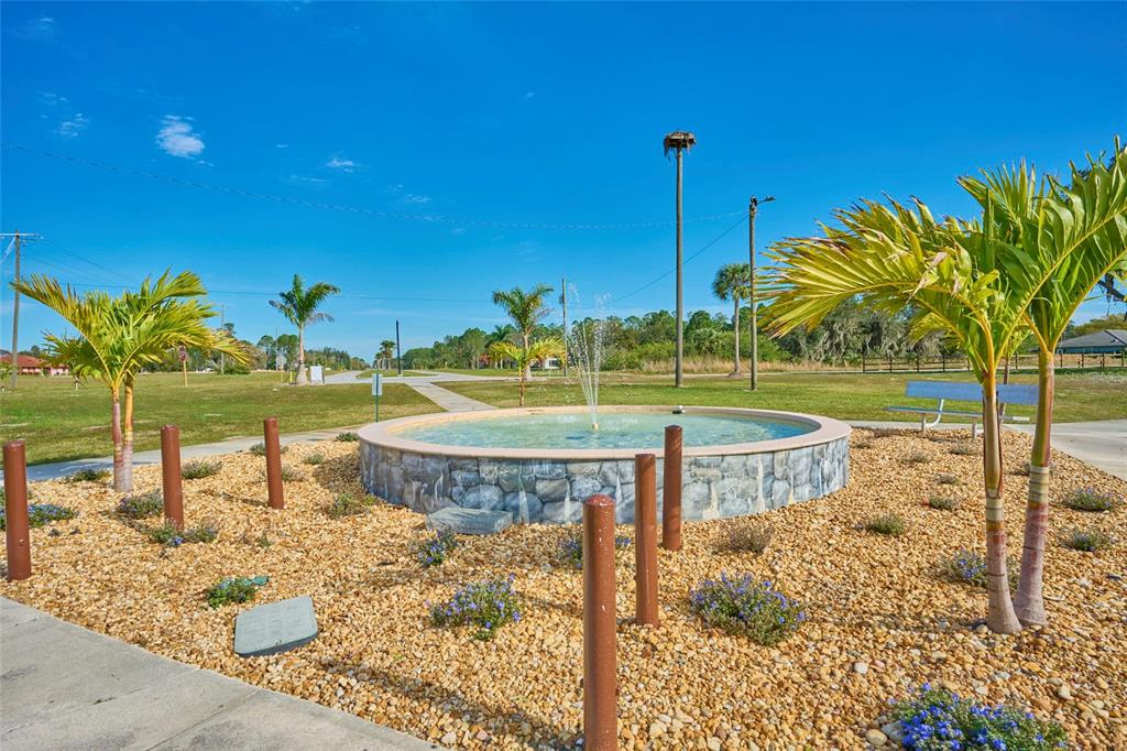 A stone-walled circular fountain sits in a landscaped area with palm trees and gravel — OLEANDER DRIVE, INDIAN LAKE ESTATES, FL