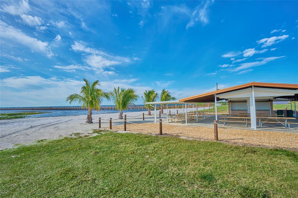 A covered picnic pavilion with tables sits on a sandy beach near a wooden pier — OLEANDER DRIVE, INDIAN LAKE ESTATES, FL
