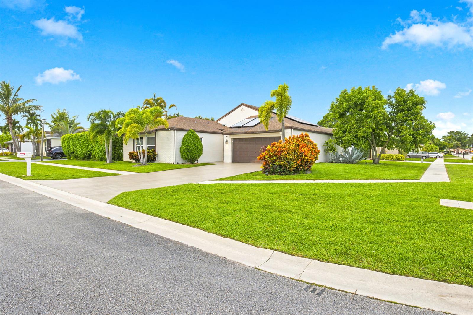 A single-story house with a brown garage, solar panels, and palm trees on a lawn — 11455 Whisper Sound Drive, Boca Raton FL 33428, BOCA RATON, FL
