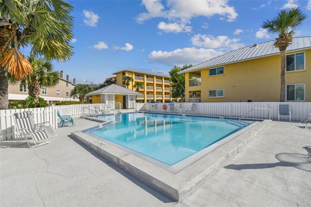 An outdoor swimming pool surrounded by a white fence and multi-story apartment buildings — 1125 PINELLAS BAYWAY S UNIT 302, TIERRA VERDE, FL