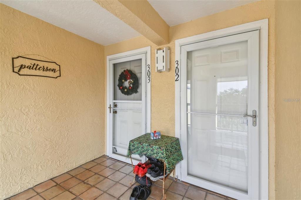 A covered entryway features two white doors with storm doors, tiled flooring, and a small table — 1125 PINELLAS BAYWAY S UNIT 302, TIERRA VERDE, FL