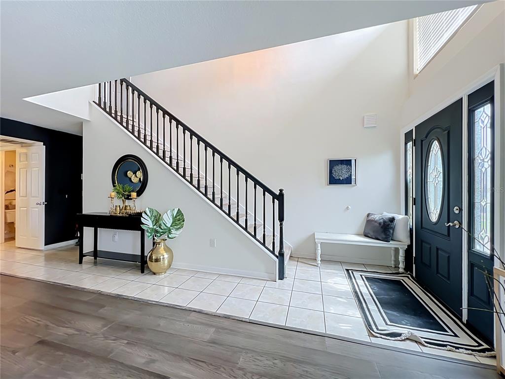 A bright entryway features a staircase with black railings, tiled flooring, and a dark front door — 410 FAIRFIELD DRIVE, SANFORD, FL