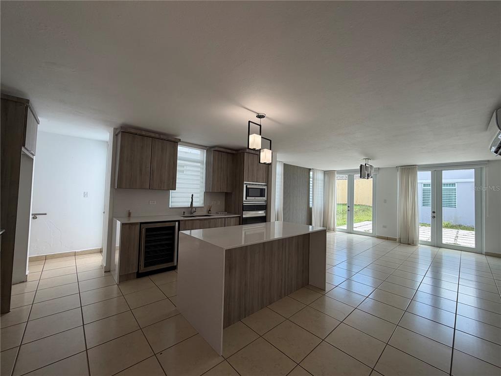 A modern kitchen with a central island, wood-toned cabinetry, and tile flooring opens to outdoors — A-70 Calle Persia PALACIO IMPERIAL, TOA ALTA, PR