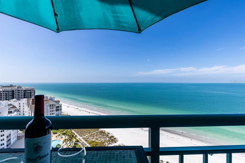 A balcony overlooks a beach and ocean with a wine bottle in the foreground — 1560 GULF BOULEVARD UNIT 1605, CLEARWATER BEACH, FL