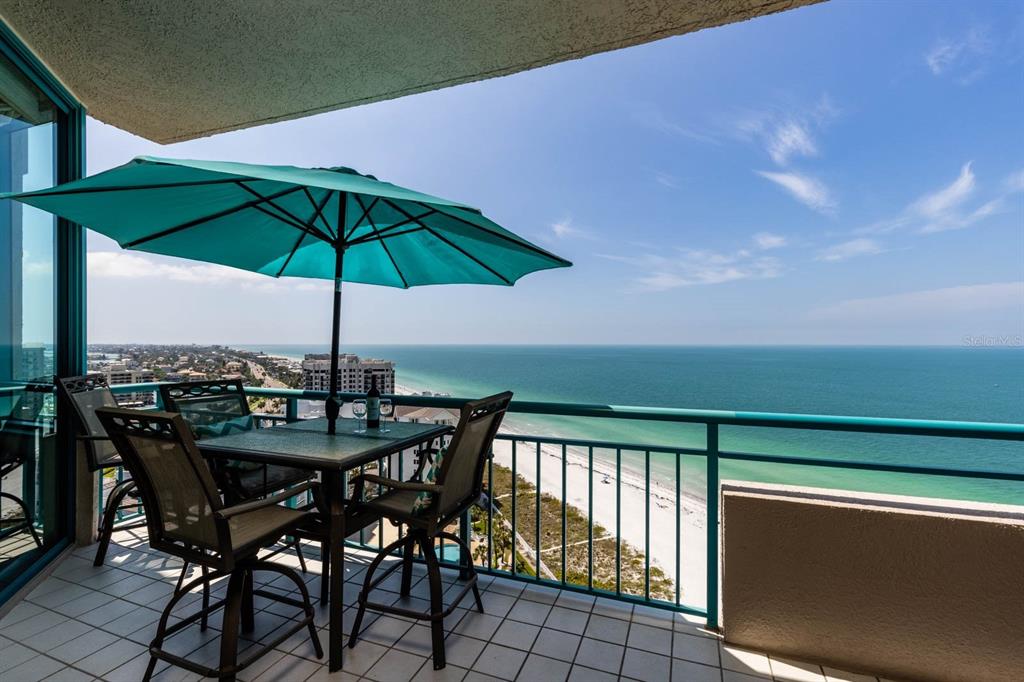 A balcony with a patio table, chairs, and umbrella overlooks a beach and the ocean — 1560 GULF BOULEVARD UNIT 1605, CLEARWATER BEACH, FL