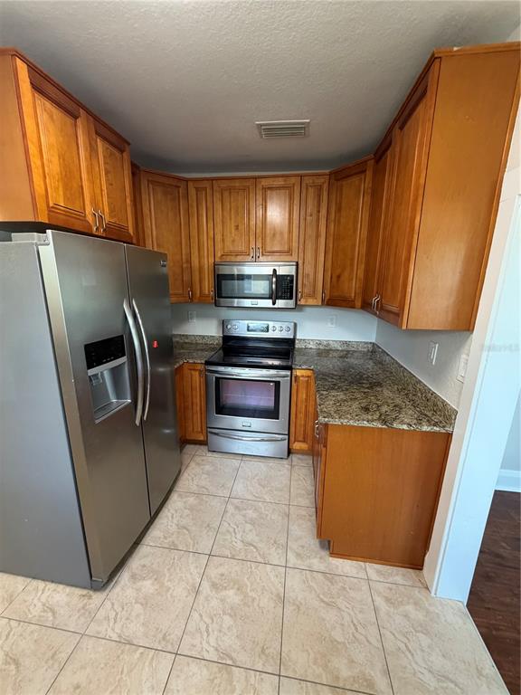 A kitchen features wood cabinets, granite countertops, stainless steel appliances, and light-colored tile flooring — 919 W PLYMOUTH STREET, TAMPA, FL