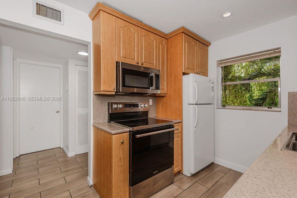 A kitchen features wood cabinets, stainless steel appliances, and light-colored countertops with tile flooring — 4111 Stirling Rd # 308, Dania Beach FL 33314, DANIA BEACH, FL
