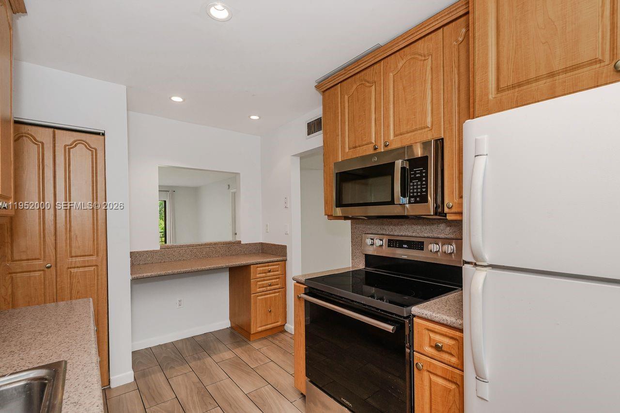 A kitchen features wood cabinets, stainless steel appliances, a pass-through window, and tile flooring — 4111 Stirling Rd # 308, Dania Beach FL 33314, DANIA BEACH, FL