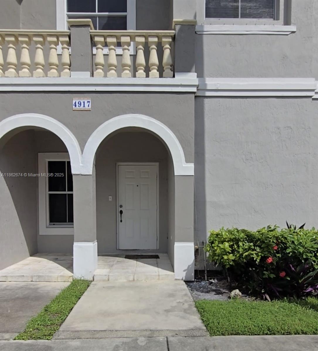 The exterior of a gray two-story townhouse features a white arched entryway and a balcony — 4917 SW 141st Ave # 4, Miramar FL 33027, MIRAMAR, FL