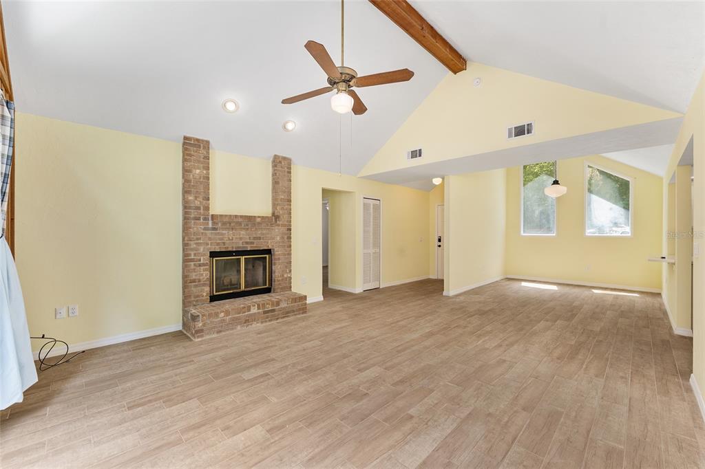 A living room with a brick fireplace, vaulted ceiling, and light-colored furniture on tiled floors — 813 SW 99TH STREET, GAINESVILLE, FL