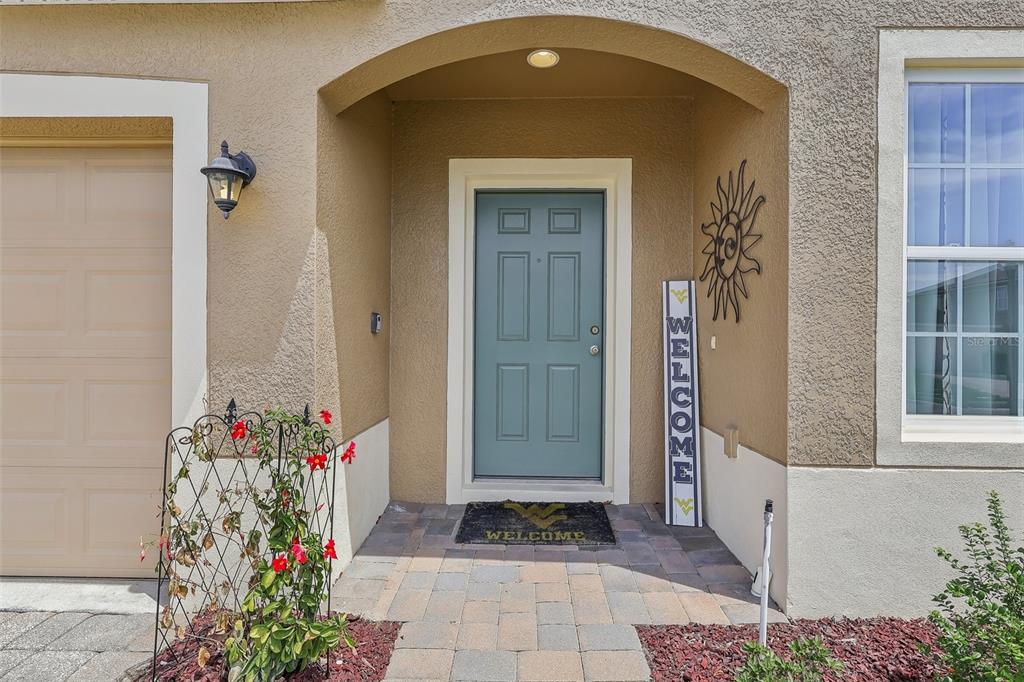 A blue front door with a welcome sign and mat sits under a covered entryway — 34046 ALAMEDA DRIVE, SORRENTO, FL