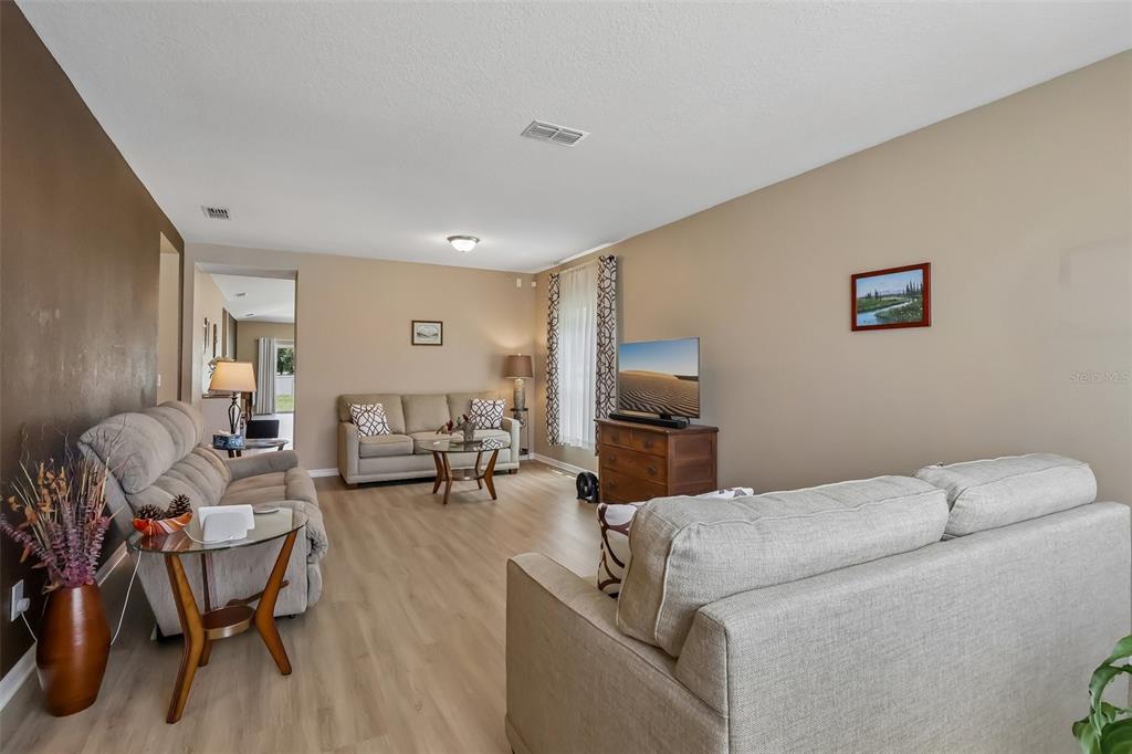A living room features light wood-look flooring, two sofas, a television, and neutral-toned walls — 34046 ALAMEDA DRIVE, SORRENTO, FL