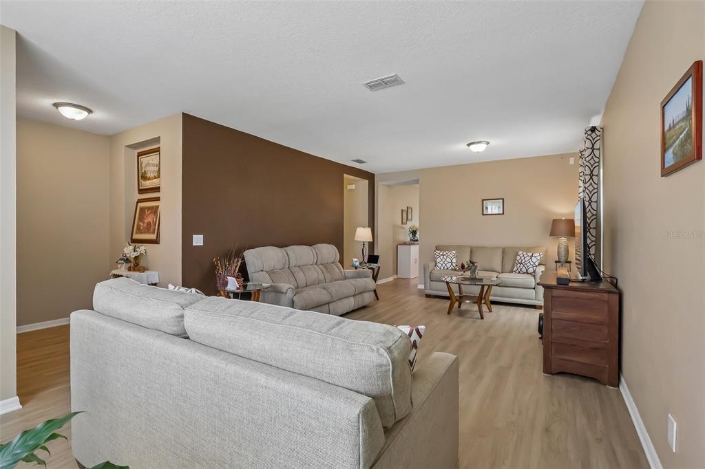 A living room features light wood-look flooring, neutral walls, and three gray sofas — 34046 ALAMEDA DRIVE, SORRENTO, FL