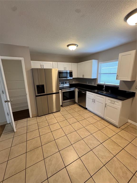 A kitchen with white cabinets, stainless steel appliances, black countertops, and light-colored tile flooring — 1801 17TH STREET, ST CLOUD, FL