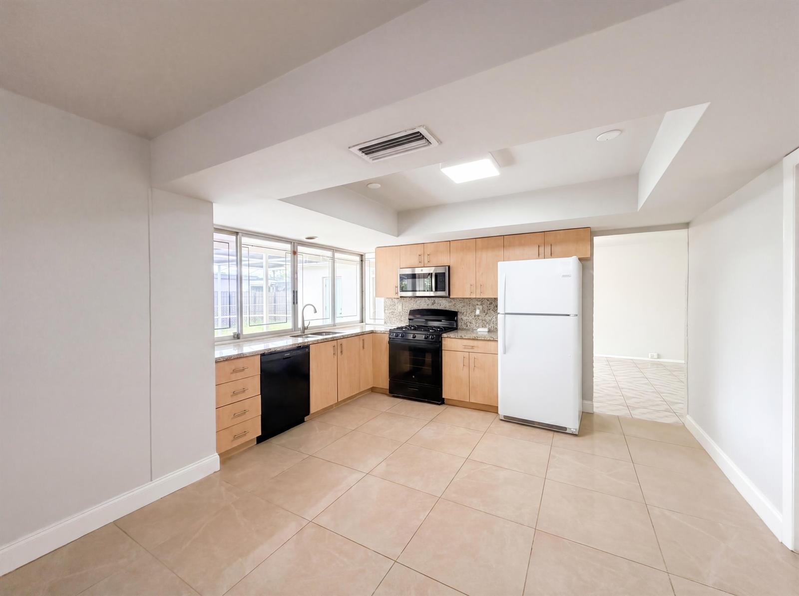 A kitchen features light wood cabinets, granite countertops, stainless steel appliances, and beige tile flooring — 7141 Harbour Boulevard, Miramar FL 33023, MIRAMAR, FL