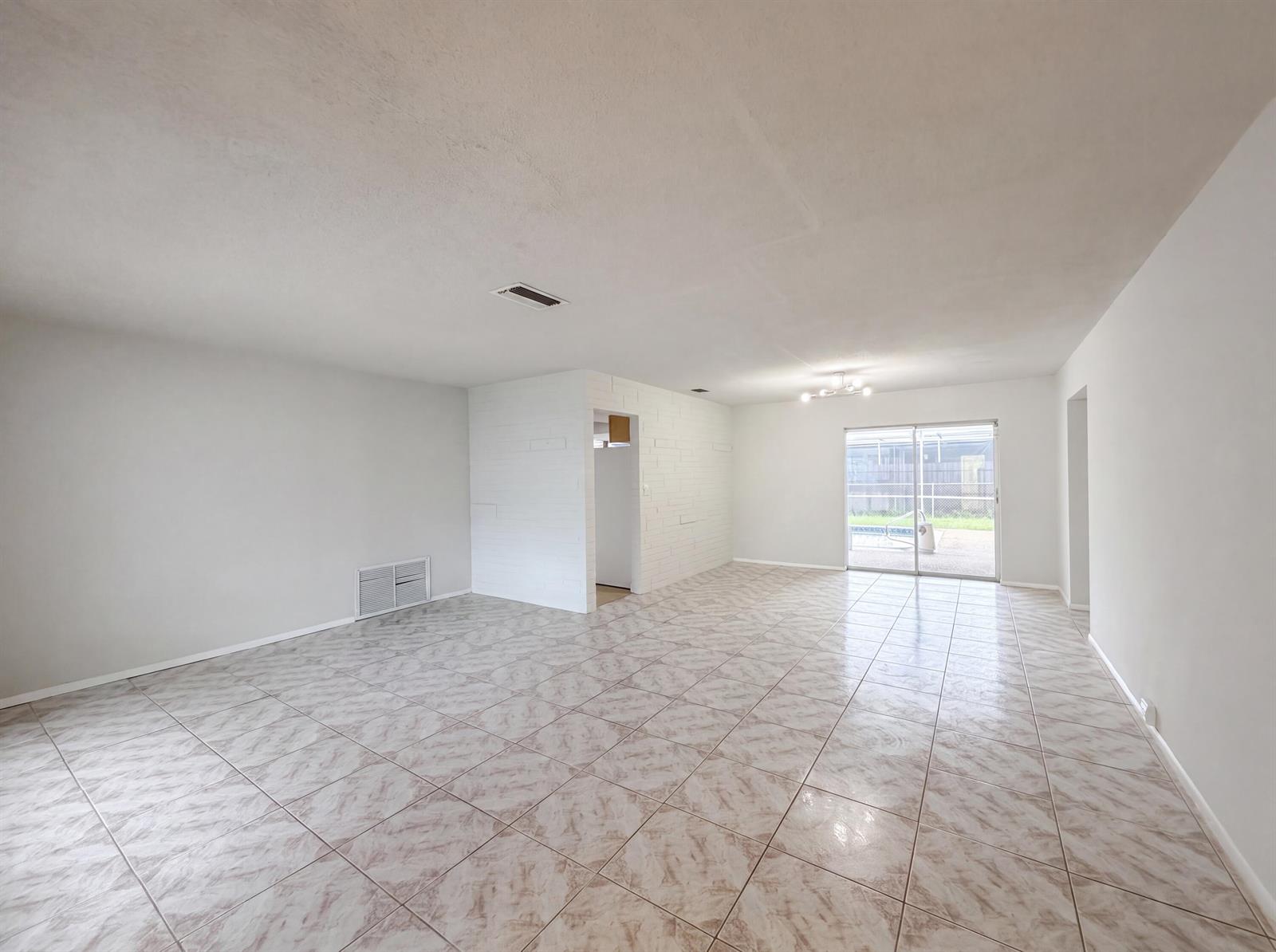 An open-concept living area features white walls, tile flooring, a brick accent wall, and sliding doors — 7141 Harbour Boulevard, Miramar FL 33023, MIRAMAR, FL