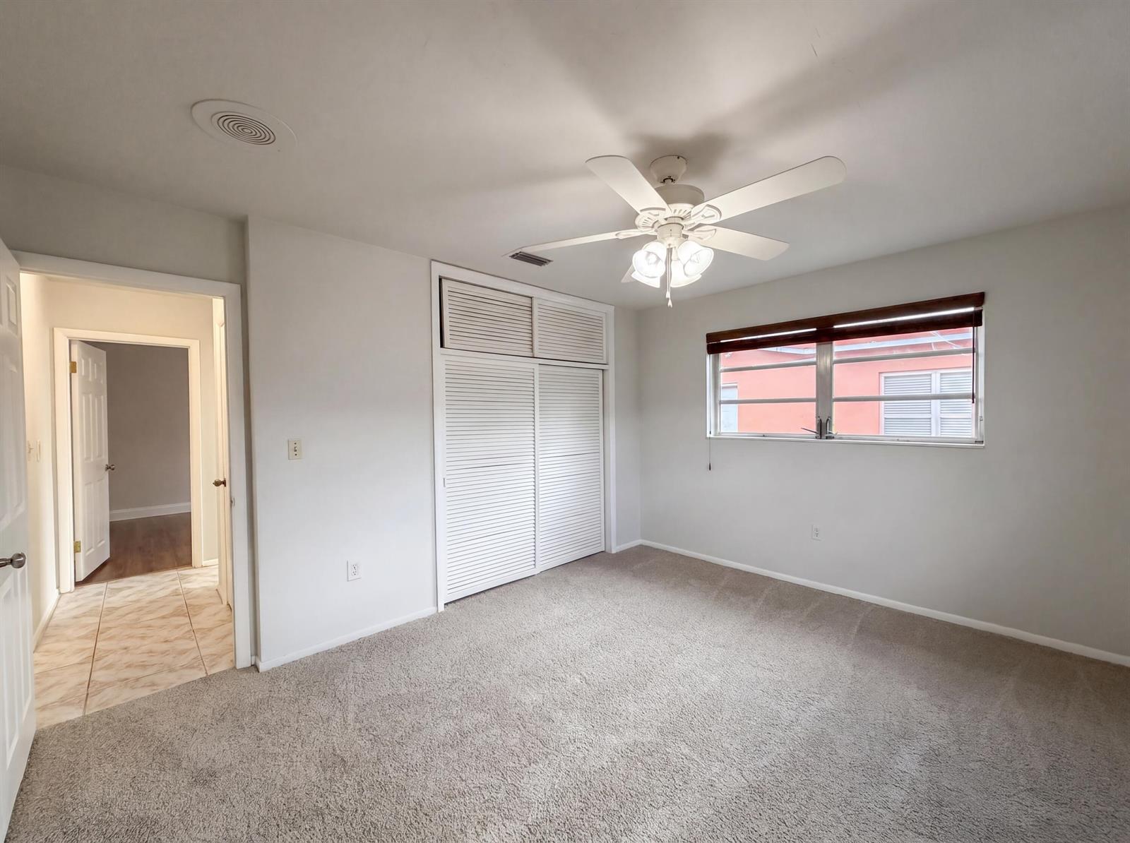 A bedroom features beige carpeting, white walls, a ceiling fan, and a white louvered closet — 7141 Harbour Boulevard, Miramar FL 33023, MIRAMAR, FL
