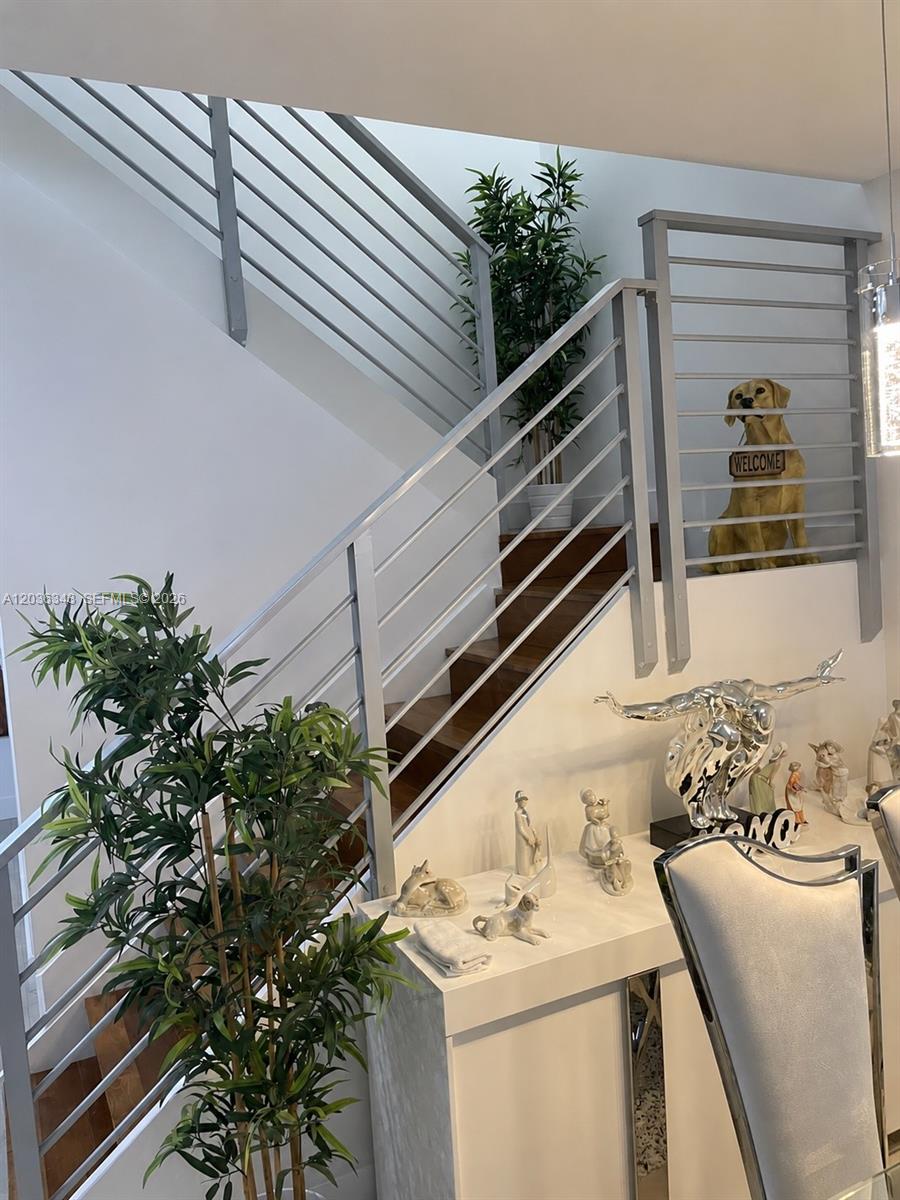 A staircase with metal railings and wooden steps is positioned behind a white console table — 7117 NW 103rd Path, Doral FL 33178, DORAL, FL